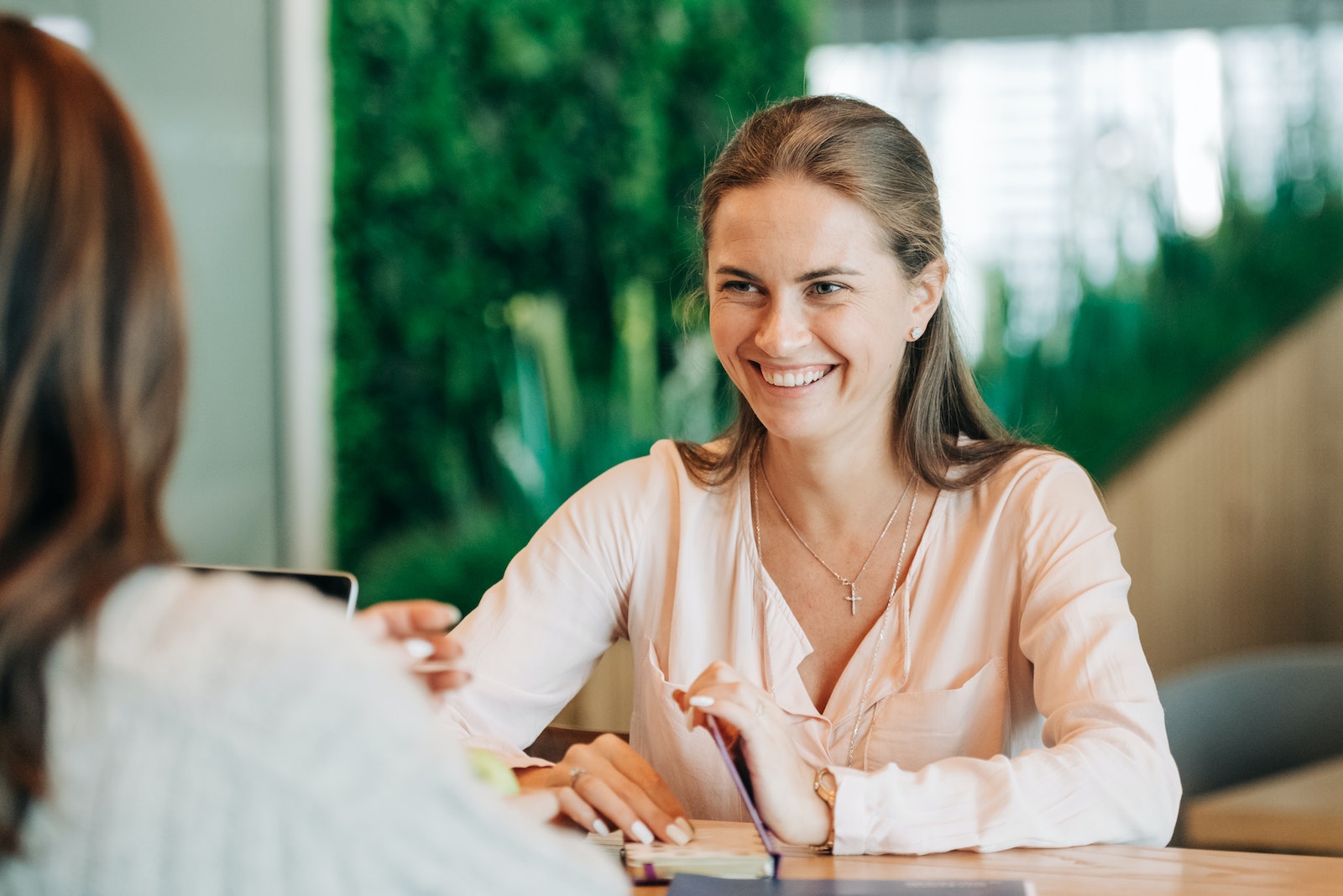 Cheerful young female speaking with crop anonymous friend on blurred background of cafe with green plants